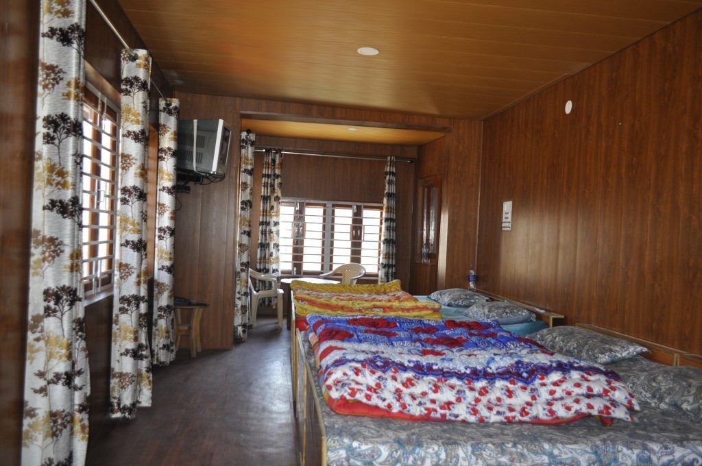 A room with a wooden ceiling, a bed with a colorful blanket, a chair, and a window with curtains.