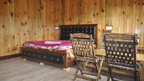 A wooden-paneled room with a bed, two wooden chairs, and a small table. - Hotel Garden Cottage & Resort Dhanaulti (Dhanaulti)