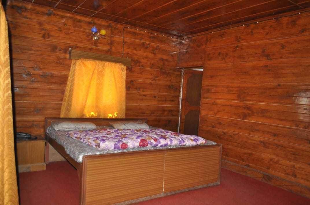 A wooden cabin bedroom with a bed, a nightstand, a mirror, and a hanging light fixture.