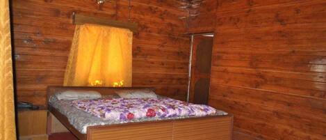 A wooden cabin bedroom with a bed, a nightstand, a mirror, and a hanging light fixture.