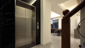 Un ascensor moderno con detalles de mármol, barandilla de madera y un área de comedor al fondo.