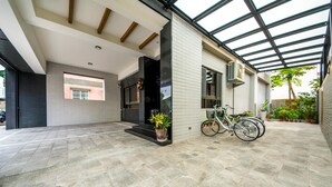 Un edificio moderno con un patio cubierto, una bicicleta estacionada afuera y una planta en maceta en los escalones.