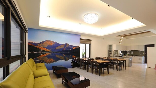 Una sala moderna con un sofá amarillo, una mesa de centro y un comedor con múltiples sillas. Un cuadro grande de montañas y un lago adorna la pared.