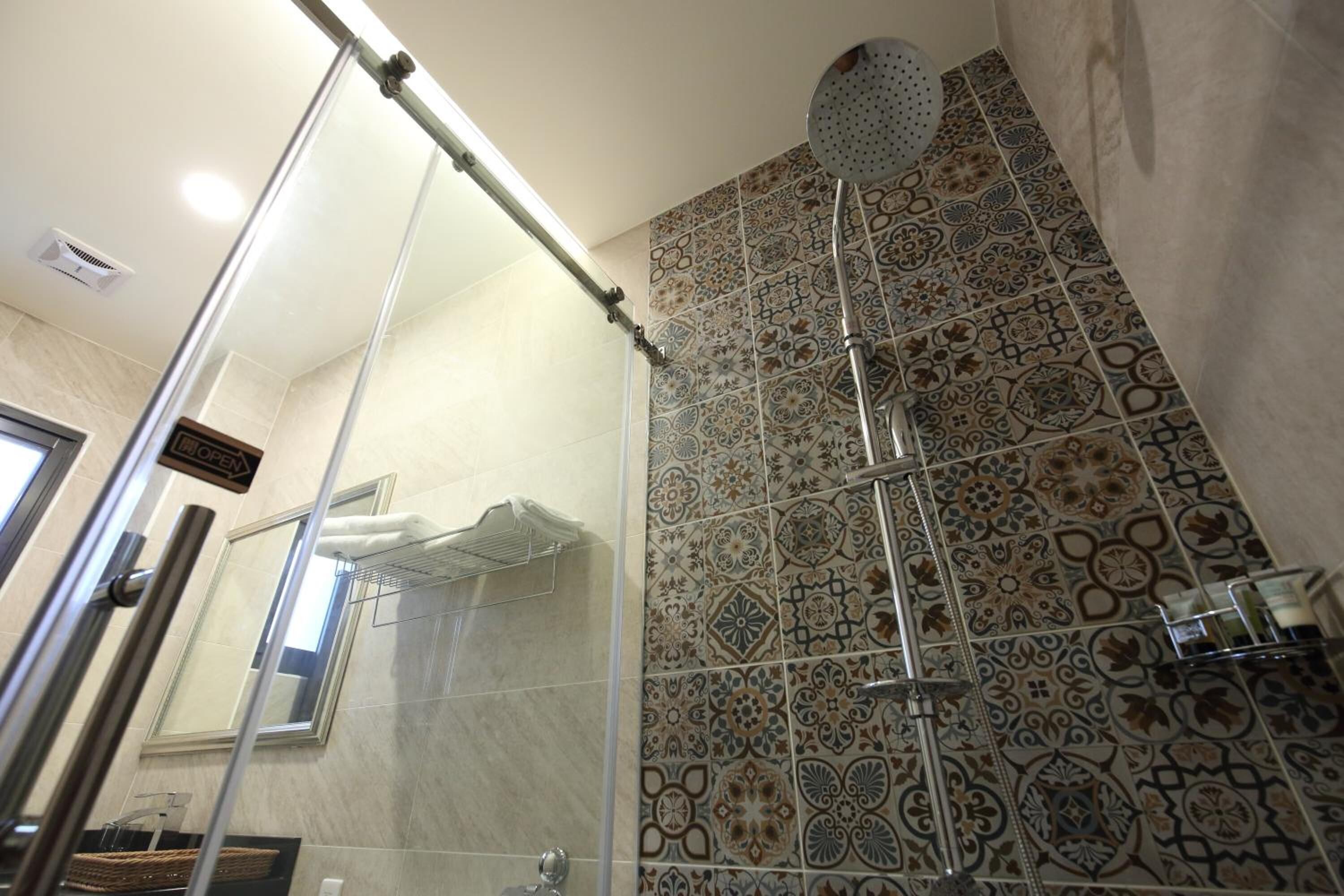 A shower with a glass door, a ceiling-mounted showerhead, and patterned tiles on the walls.