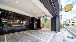 Entrada de hotel con pavimento de baldosas, puerta de vidrio y un letrero.