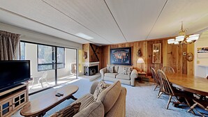 A spacious living room with a fireplace, a dining area with a wooden table and chairs, and a large window providing natural light. - Great 2 Bedroom Condo with Amazing Views! Access to Hot Tubs and Heated Pool! (Unit 307 at 1849) by RedAwning (Mammoth Lakes)