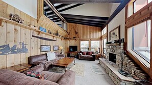 A spacious living room with wooden walls, a stone fireplace, and a large window providing natural light.