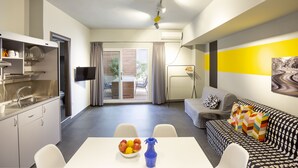 Een modern appartement met keuken, eethoek en woonkamer. Het heeft een eettafel met fruit, een bank en een televisie.