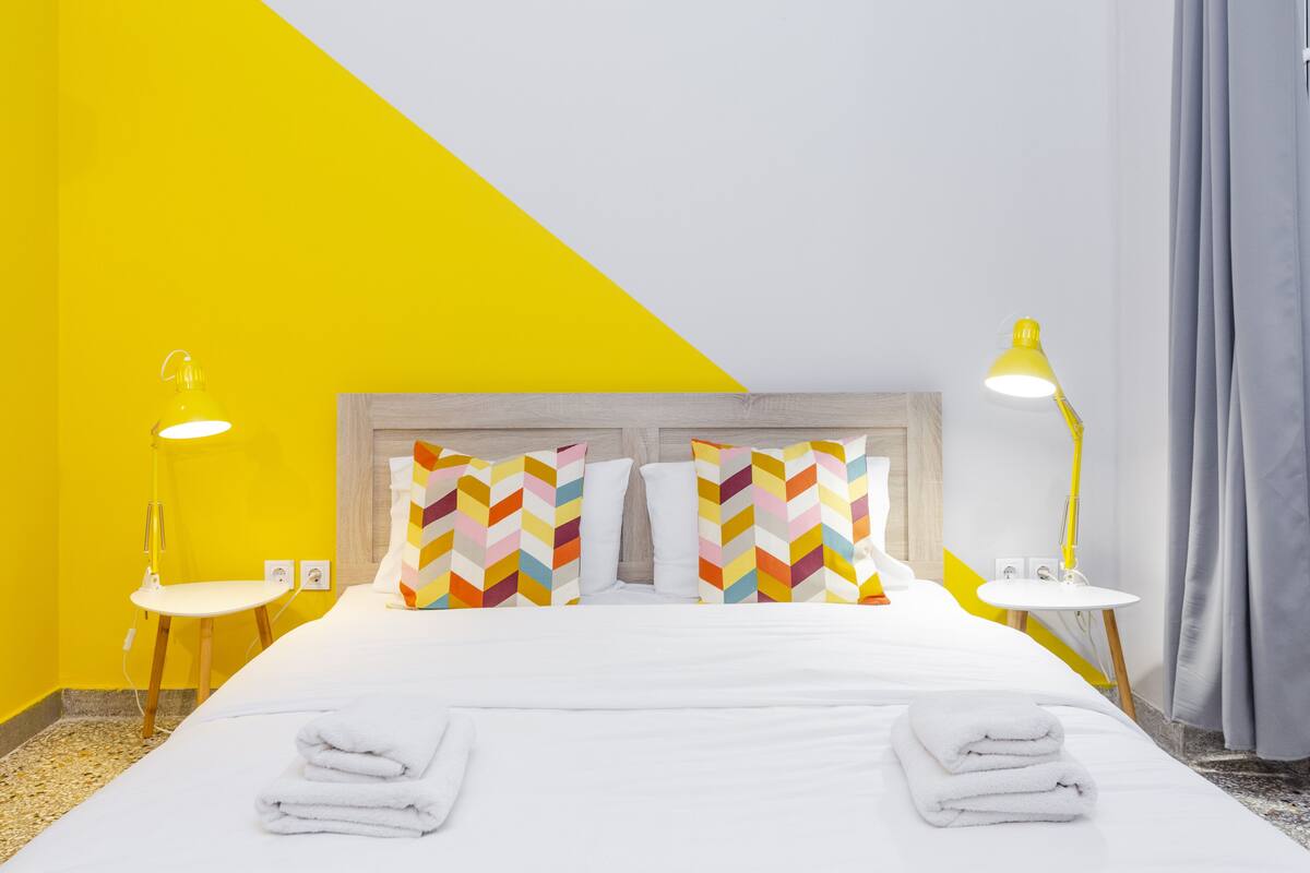 A hotel room with a bed, two bedside lamps, a chair, and a small table.