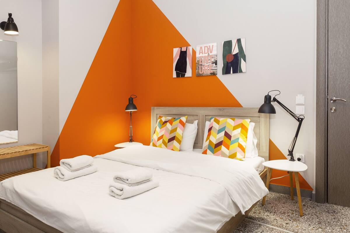 A modern hotel room with a bed, two bedside lamps, a small round table, and a wall with geometric patterns and artwork.
