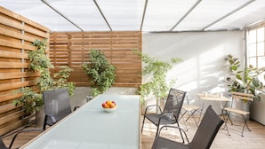 Een overdekt terras met een glazen tafel, stoelen en potplanten.