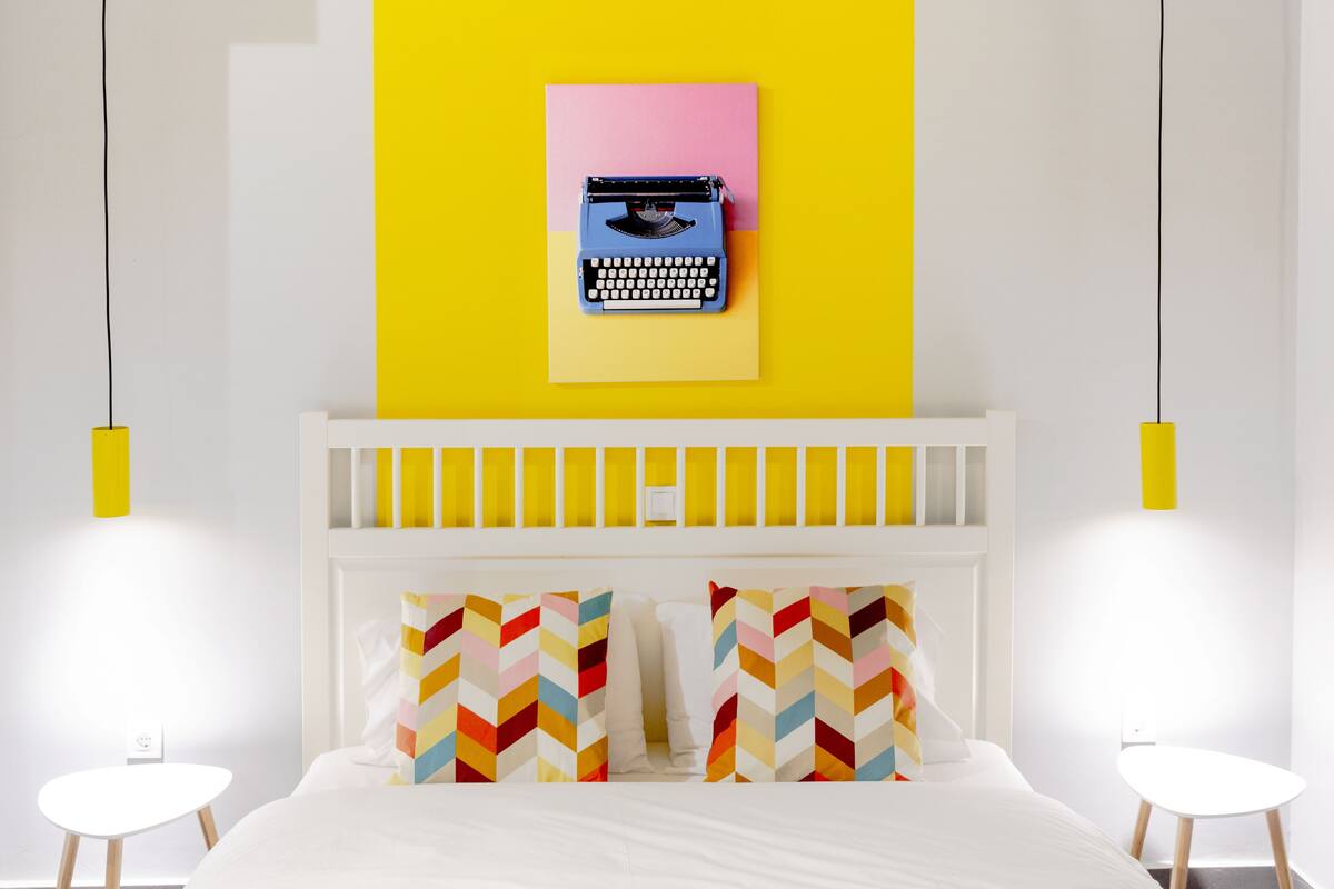 A modern bedroom with a bed, two side tables, a white headboard, and a wall-mounted typewriter.