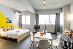 Ein modernes Hotelzimmer mit einem Bett, einer Couch, einem Esstisch und einem Fernseher.