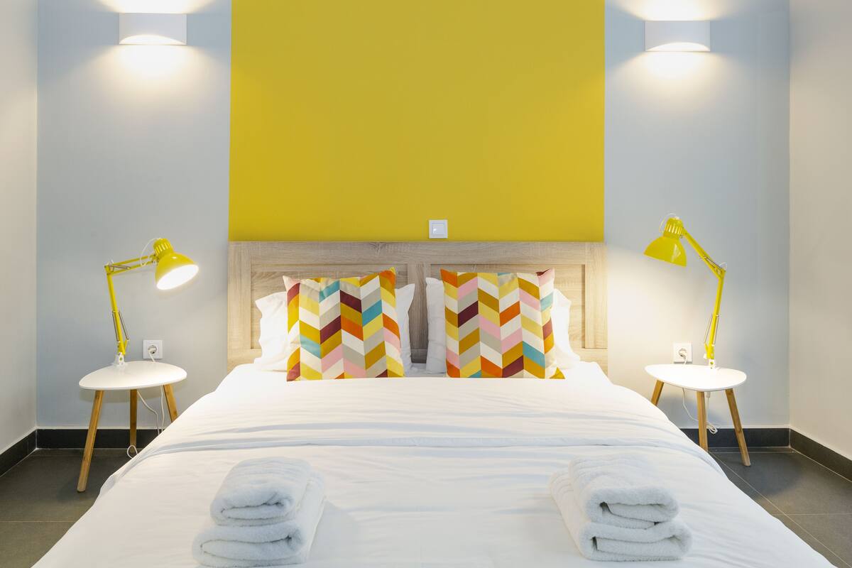 A hotel room with a bed, two bedside tables, two lamps, and a large window with yellow curtains.