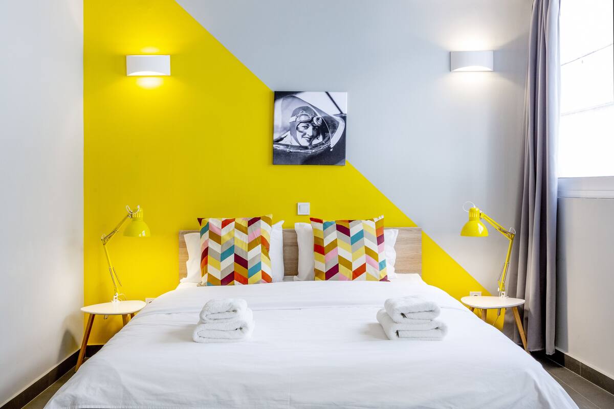 A hotel room with a bed, two bedside tables, a wall-mounted picture, and a window with curtains.