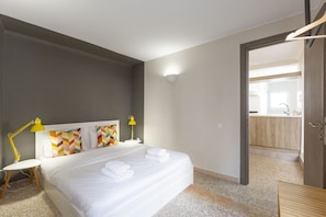 Habitación de hotel con una cama grande, dos lámparas de noche, una mesita de noche blanca y un colorido arreglo de almohadas.