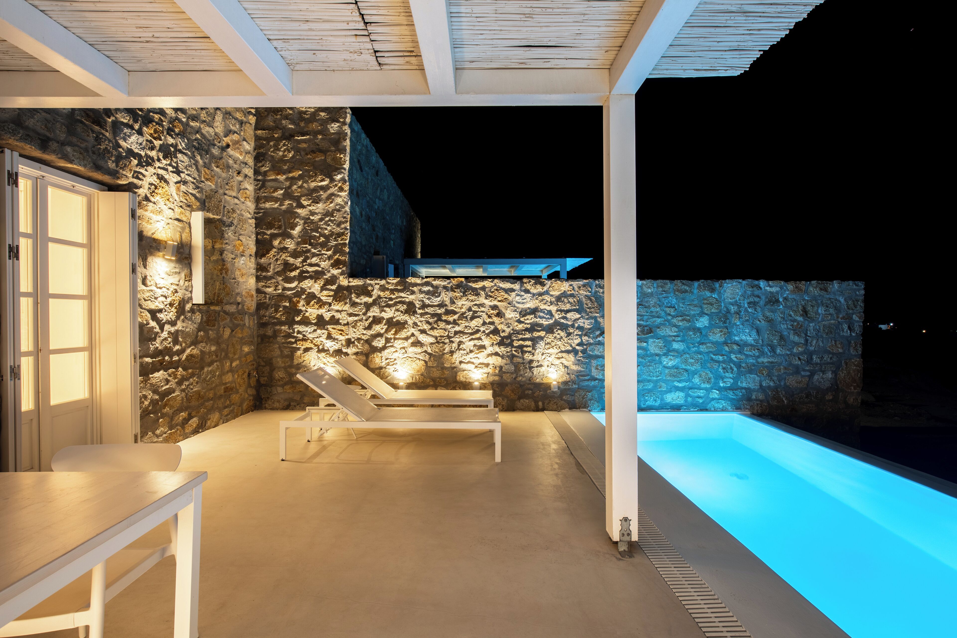 A modern outdoor pool area with stone walls, a lounge chair, and a table.