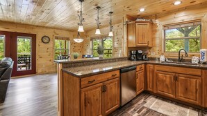 A wooden cabin kitchen with granite countertops, wooden cabinets, and a built-in dishwasher. - All Decked Out 4 Bedroom Cabin by RedAwning (Sevierville)