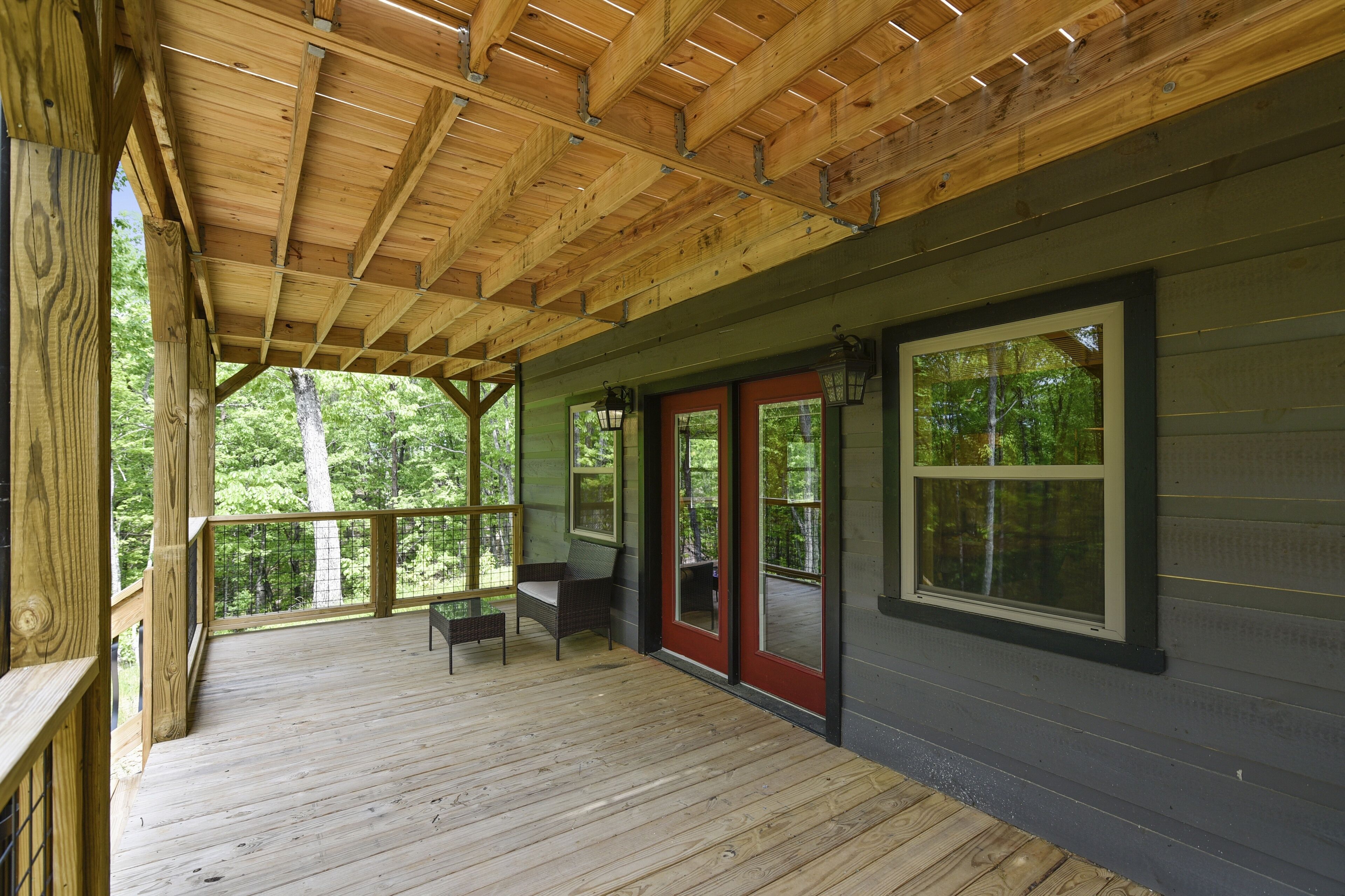 A covered wooden deck with a bench and a door leading to a room.