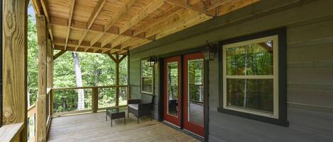 A covered wooden deck with a bench and a door leading to a room.