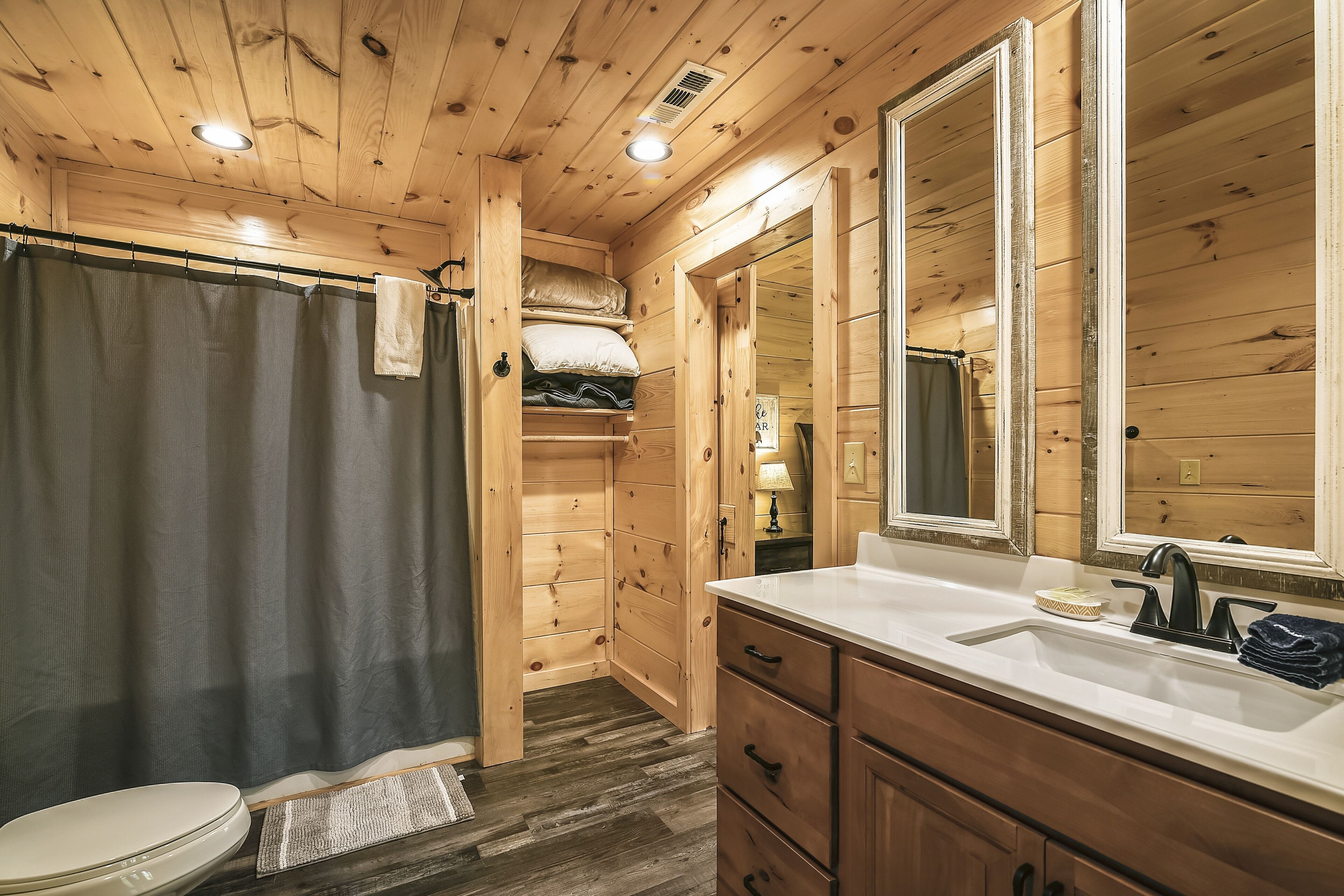 A wooden cabin bathroom with a shower curtain, a sink with a mirror, and wooden cabinets.