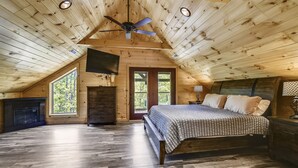 A bedroom with a wooden ceiling, a bed, a TV, and a fireplace. - All Decked Out 4 Bedroom Cabin by RedAwning (Sevierville)