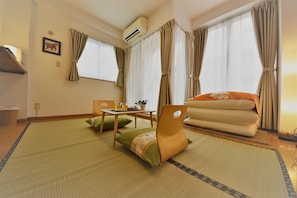 A room with tatami mats, a futon bed, a table with a plant, and a chair. - Ukishima Inn (Naha)