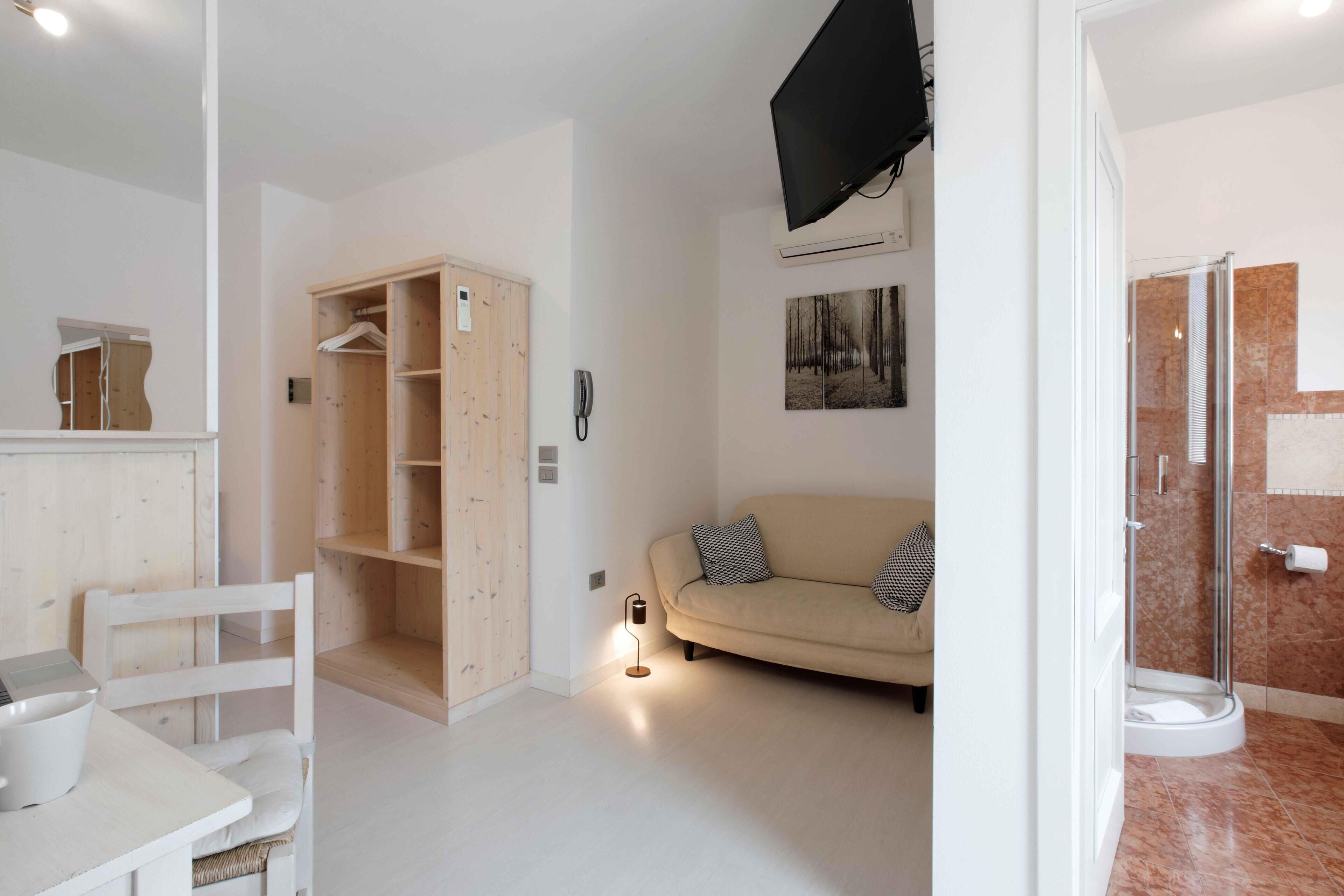 Una sala de estar moderna con un sofá, un armario de madera, un televisor montado en la pared y una zona de ducha.