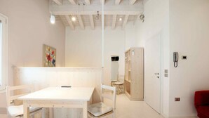 Une pièce avec une table et des chaises blanches, un meuble en bois, une chaise rouge et un tableau accroché au mur.
