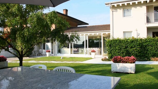 Un espace extérieur aménagé avec une table et des chaises, une salle à manger fermée par des baies vitrées et une pelouse bien entretenue.
