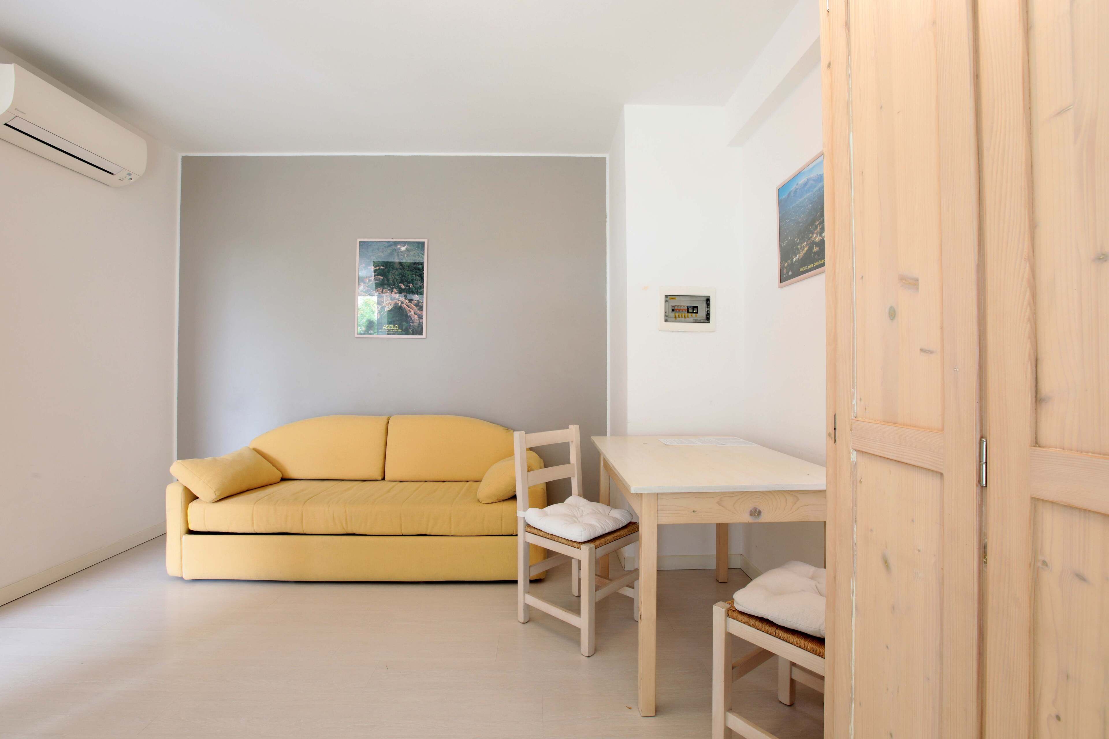 A room with a yellow sofa, a wooden chair, a small wooden table, and a wardrobe.