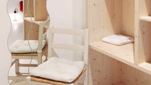 Une pièce comprenant une armoire en bois, une chaise blanche avec un coussin et un miroir qui reflète une partie de la pièce.