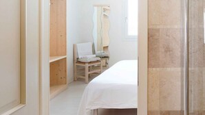 Une chambre à coucher comprenant un lit, une armoire en bois, une chaise et une cabine de douche en verre.