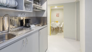 A modern kitchen with stainless steel appliances, a coffee maker, and a sink. There is a dining area with a white table and chairs visible through an open doorway. - Kavalloti Place (Athens)