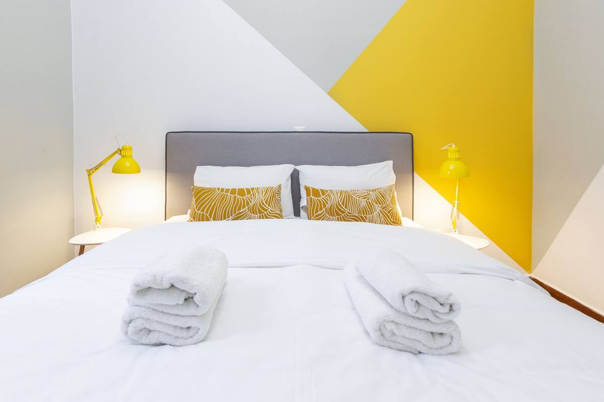 A neatly made bed with white linens and two rolled towels at the foot of the bed.