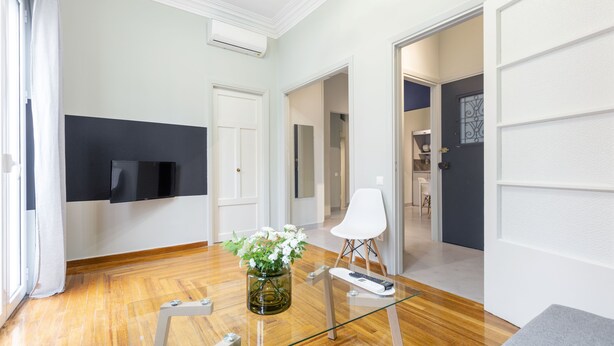 A modern living room with a wooden floor, a glass coffee table, a white chair, and a vase with flowers. - Kavalloti Place (Athens)