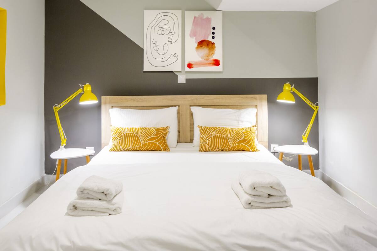 A neatly made bed with two pillows, two bedside lamps, and two towels on the bed.