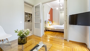 A modern hotel room with a wooden floor, a bed, a TV, a glass coffee table, a remote control, and a vase with flowers. - Kavalloti Place (Athens)