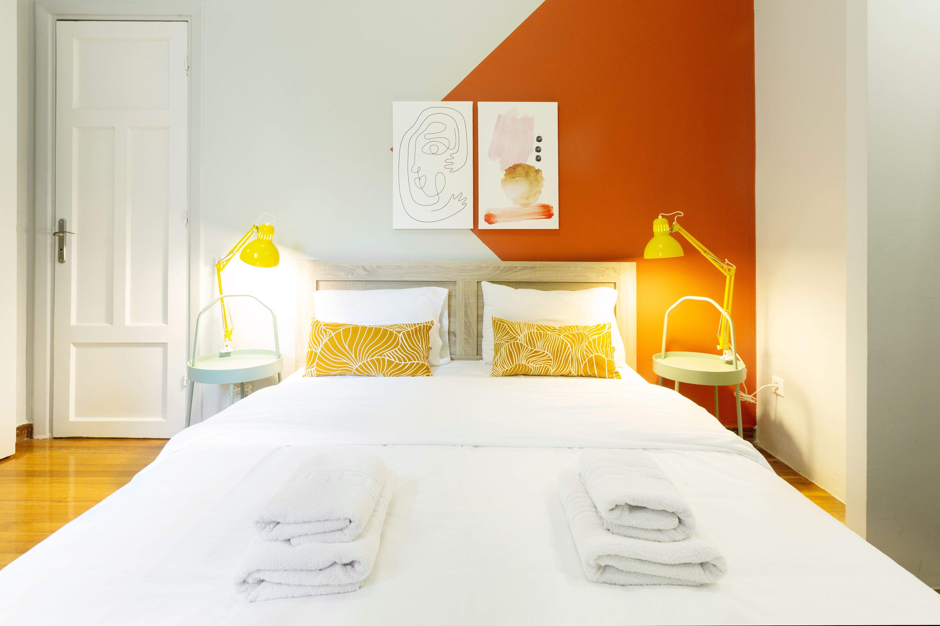 Une chambre d’hôtel avec un lit, deux lampes de chevet, une porte blanche et un mur orné d’un tableau.
