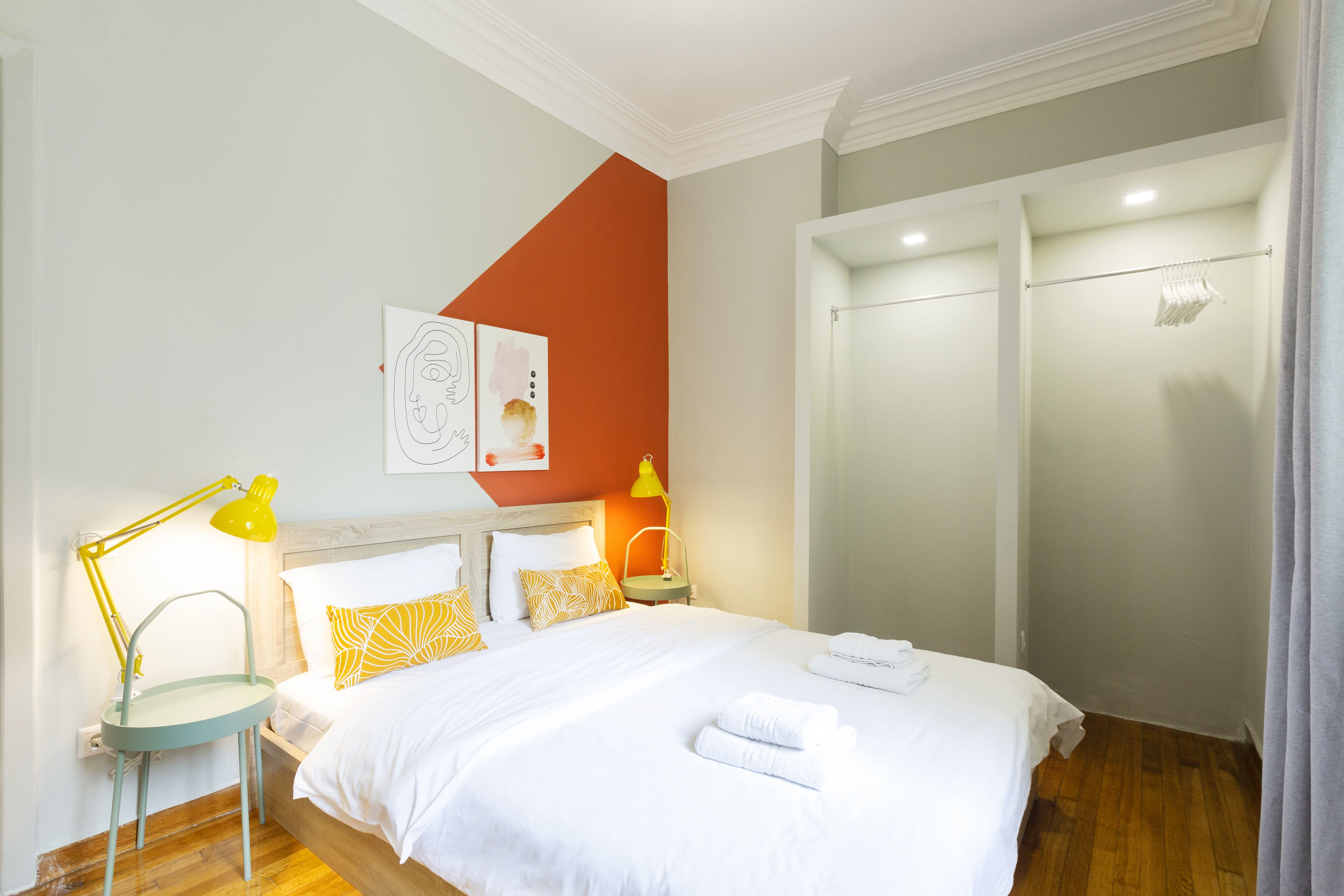 A hotel room with a bed, a nightstand with a lamp, a wardrobe, and a wall with artwork.
