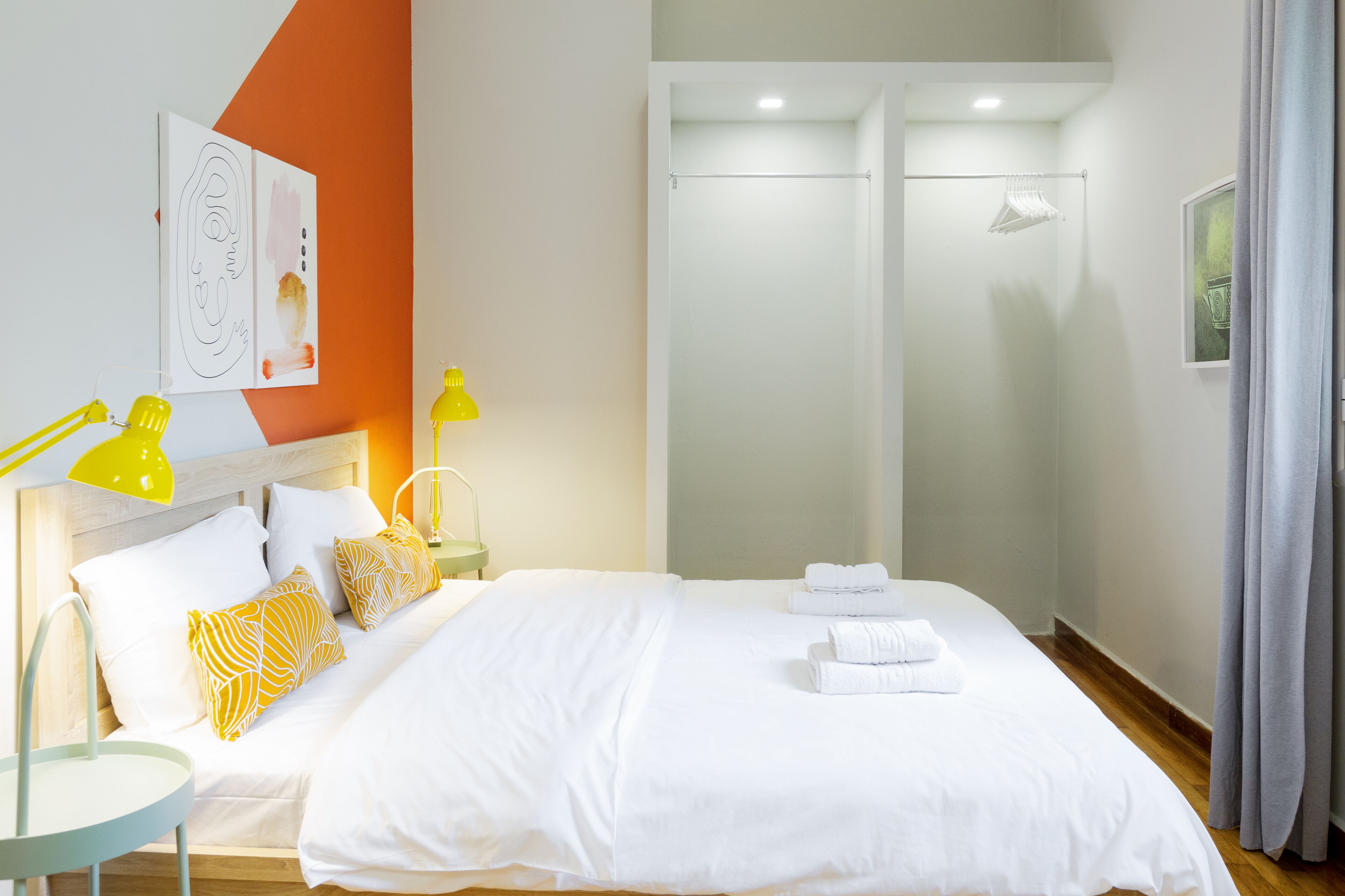 Una habitación de hotel moderna con una cama grande, ropa de cama blanca, cabecera de madera, mesita de noche con lámpara y zona de ducha.