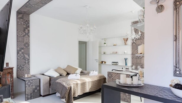 Un dormitorio moderno con cama, mesitas de noche, televisor, candelabro y baño con espejo y estanterías.
