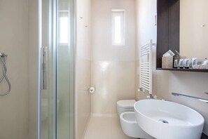 Un baño moderno con ducha envuelta en vidrio, inodoro blanco y un lavamanos grande y blanco.