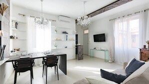 Una sala de estar moderna con comedor, televisor montado en la pared y candelabro.