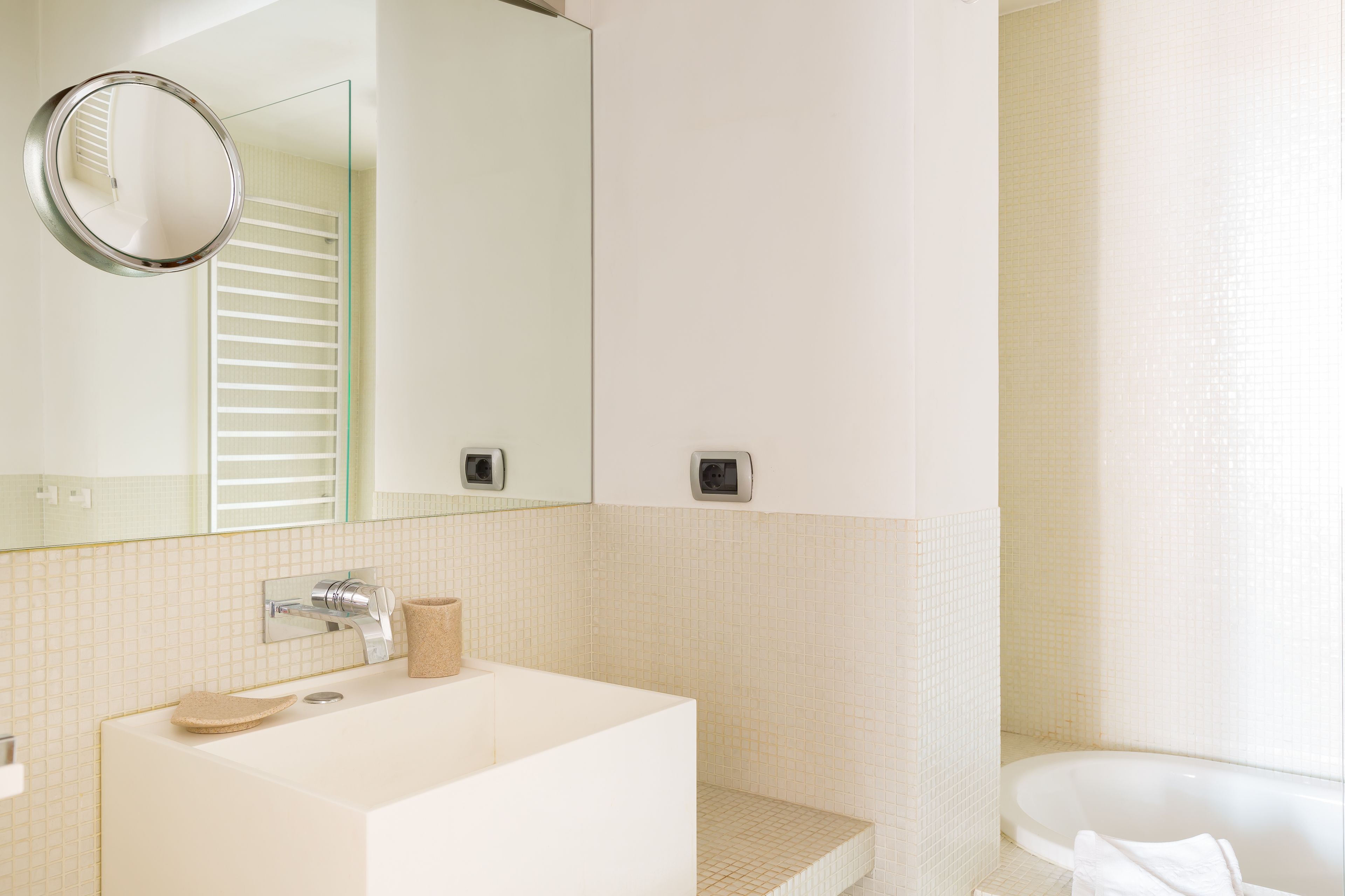 A modern bathroom with a large mirror, a sink, and a bathtub.
