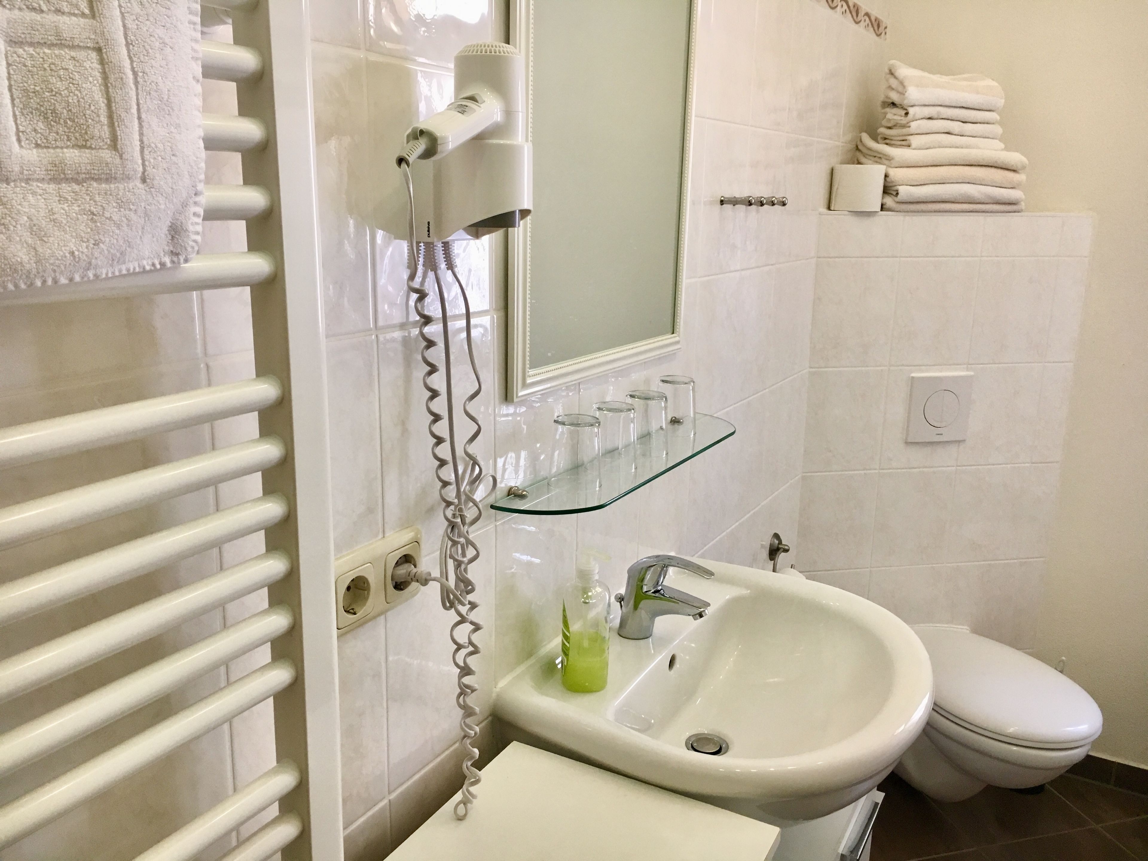 A bathroom with a white sink, a toilet, a glass shelf with toiletries, and a towel rack.