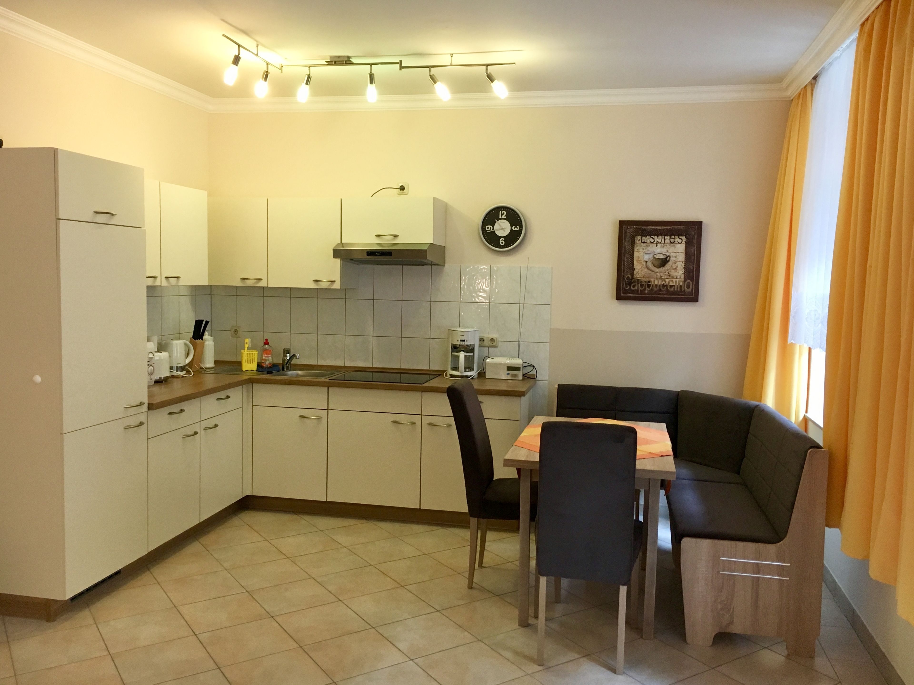 A compact kitchen with white cabinets, a built-in oven, a coffee machine, and a dining area with a table and chairs.
