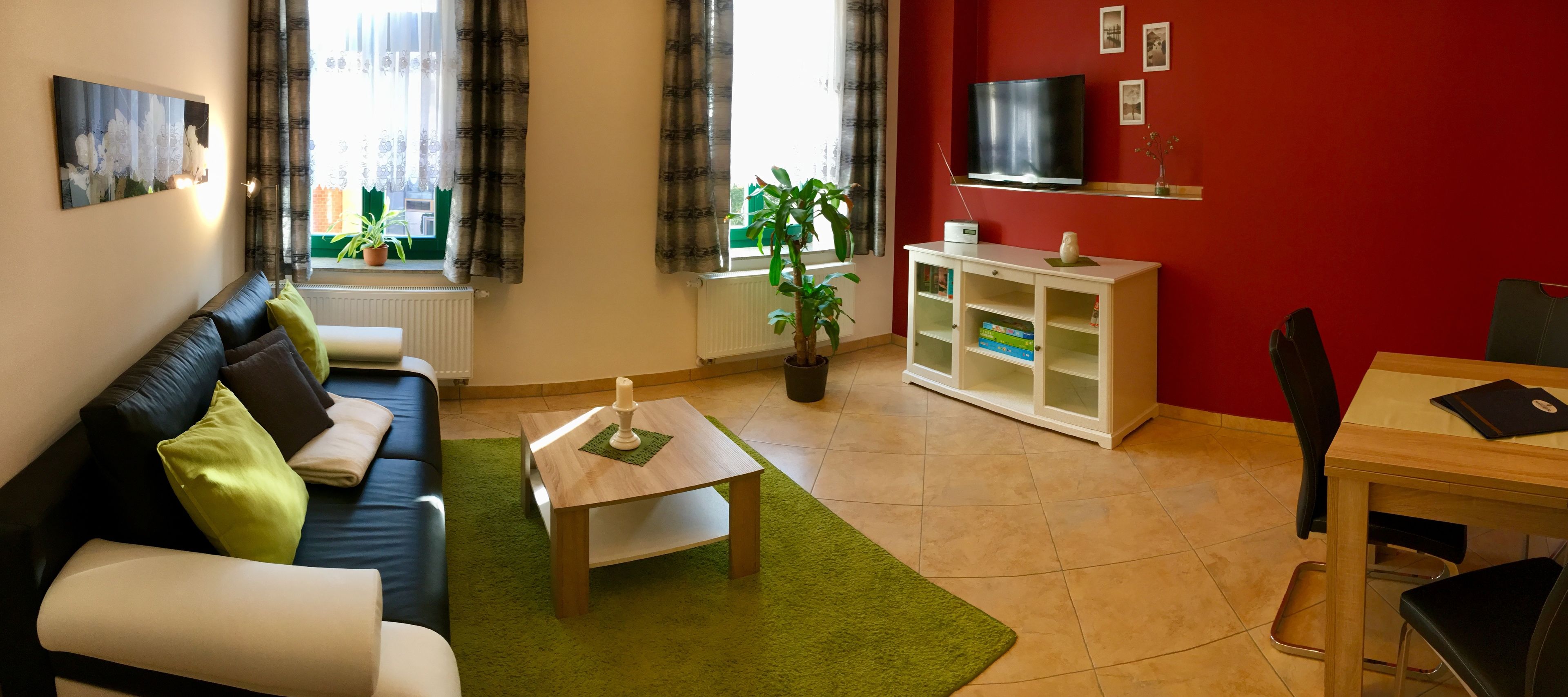 A living room with a sofa, coffee table, and a TV on a red wall.