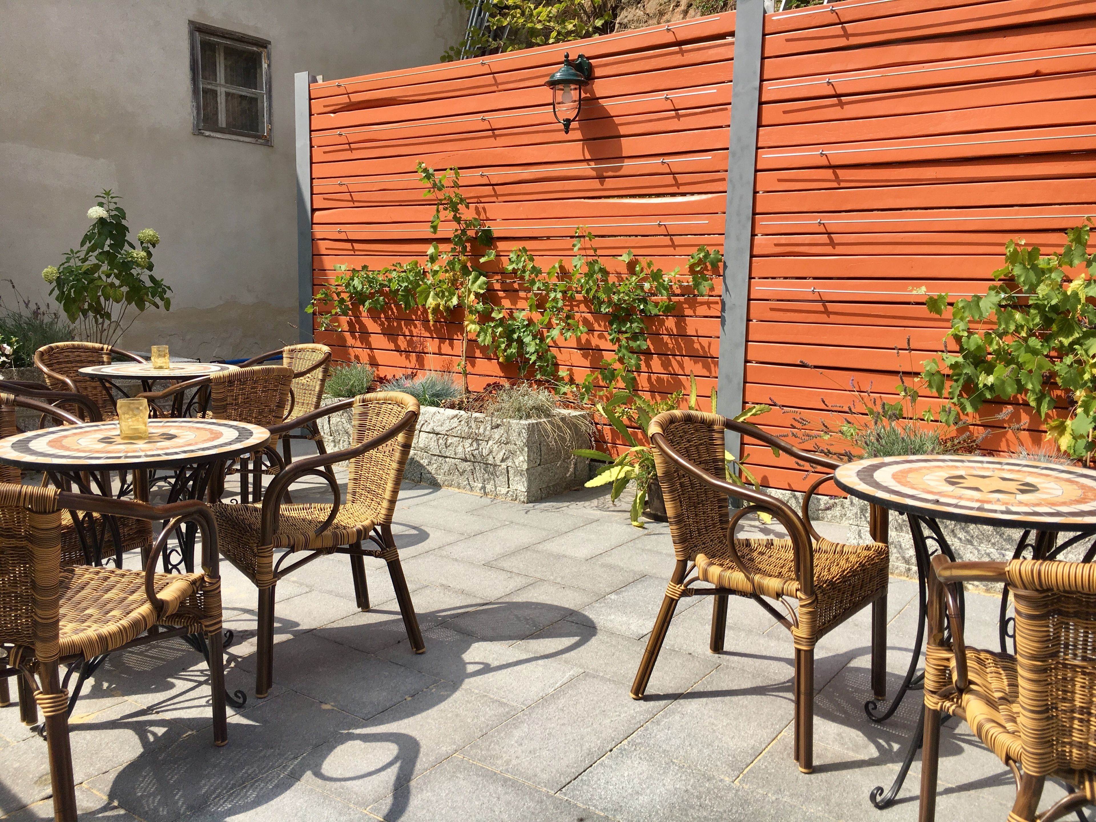 Outdoor wicker furniture with round tables, a wooden fence, and climbing plants.
