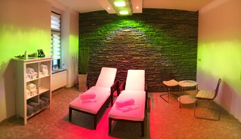 Un cuarto de spa con dos camillas de masaje, una pared de piedra, un estante con toallas y una mesita con una silla.